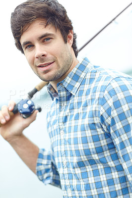 Buy stock photo A handsome young fisherman standing at the lake while carrying his gear