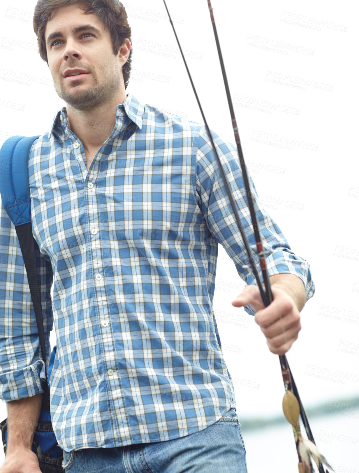 Buy stock photo A handsome young fisherman strolling near the lake while carrying his gear