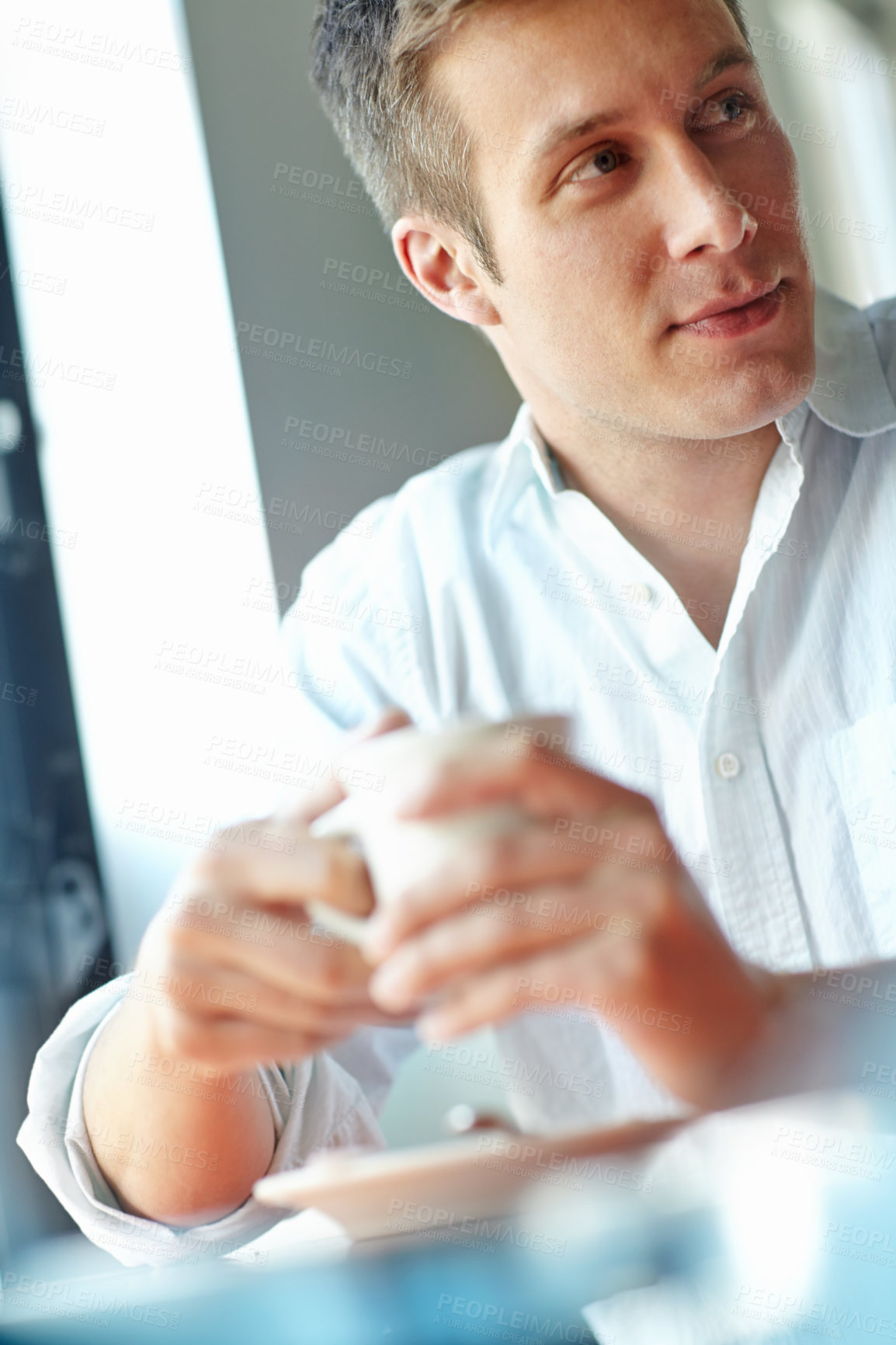 Buy stock photo A thoughtful young man relaxing with a cup of coffee at a bistro