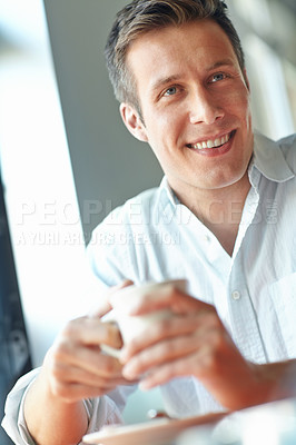 Buy stock photo A smiling young man looking away while enjoying a cup of coffee