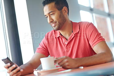 Buy stock photo A young man reading a text message while enjoying a cup of coffee