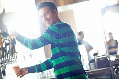 Buy stock photo A handsome young bartender pouring a pint of ale and giving you a wide smile