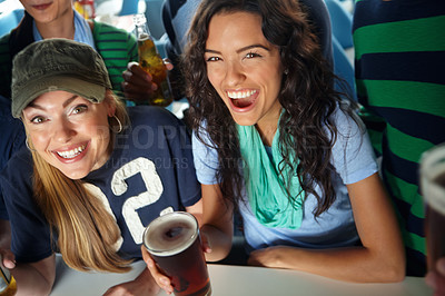 Buy stock photo Two gorgeous girls enjoying drinks and watching the game with friends