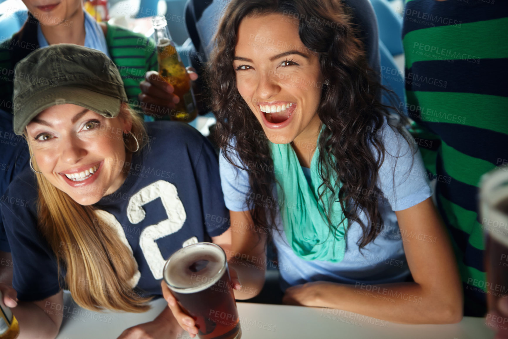 Buy stock photo Two gorgeous girls enjoying drinks and watching the game with friends