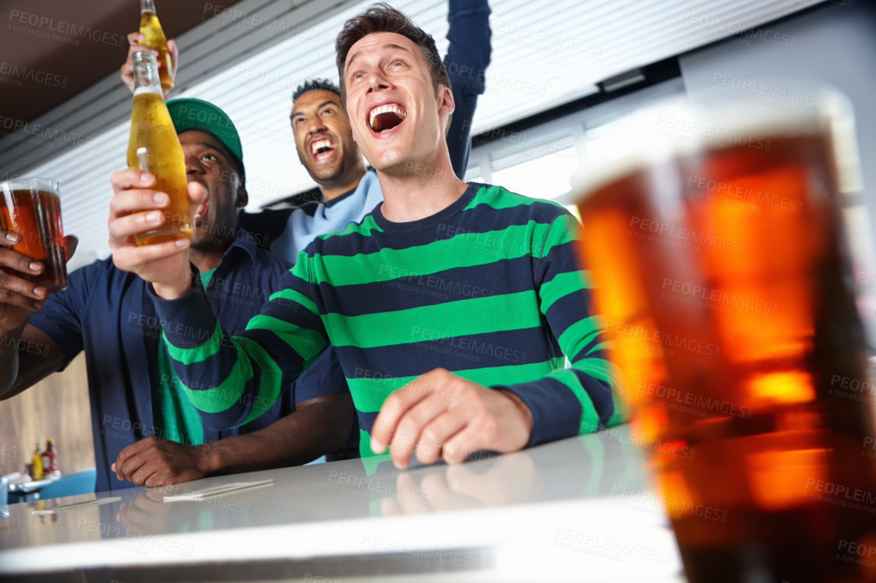 Buy stock photo Low view of a group of friends cheering on their favourite sports team at the bar