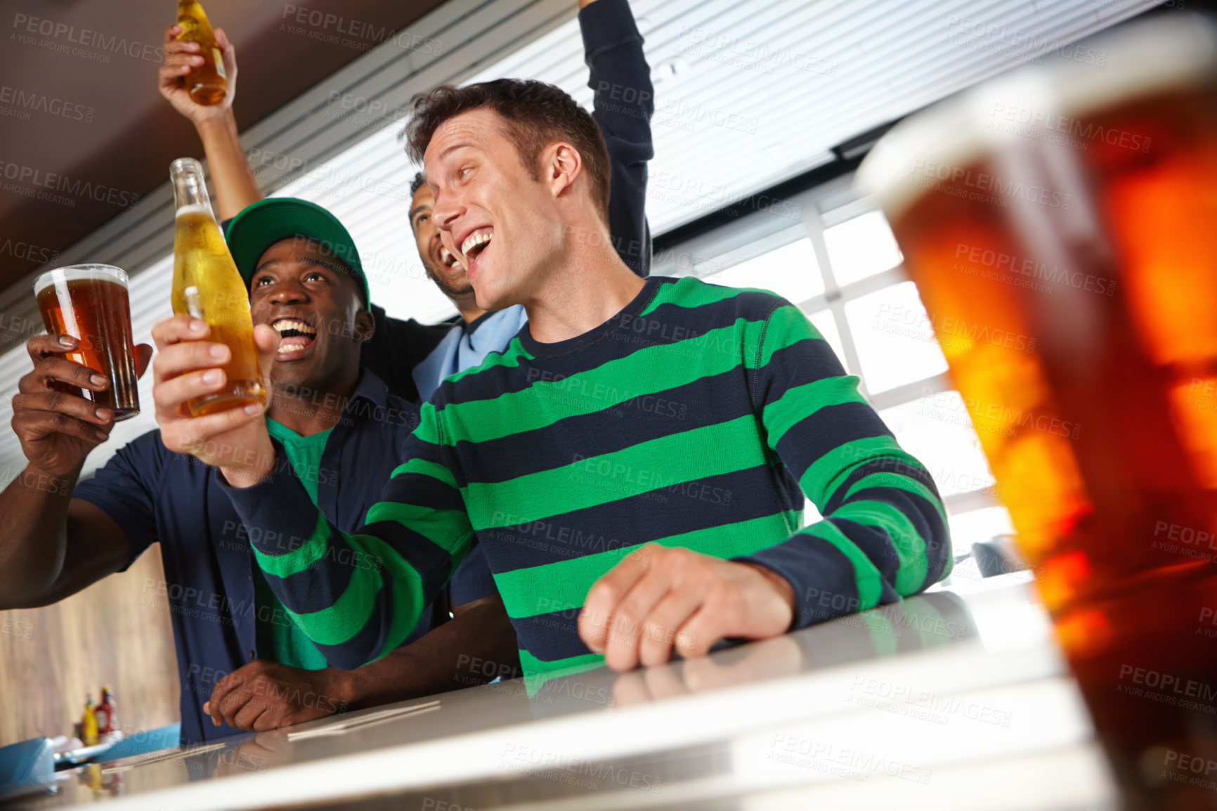 Buy stock photo Low view of a group of friends cheering on their favourite sports team at the bar