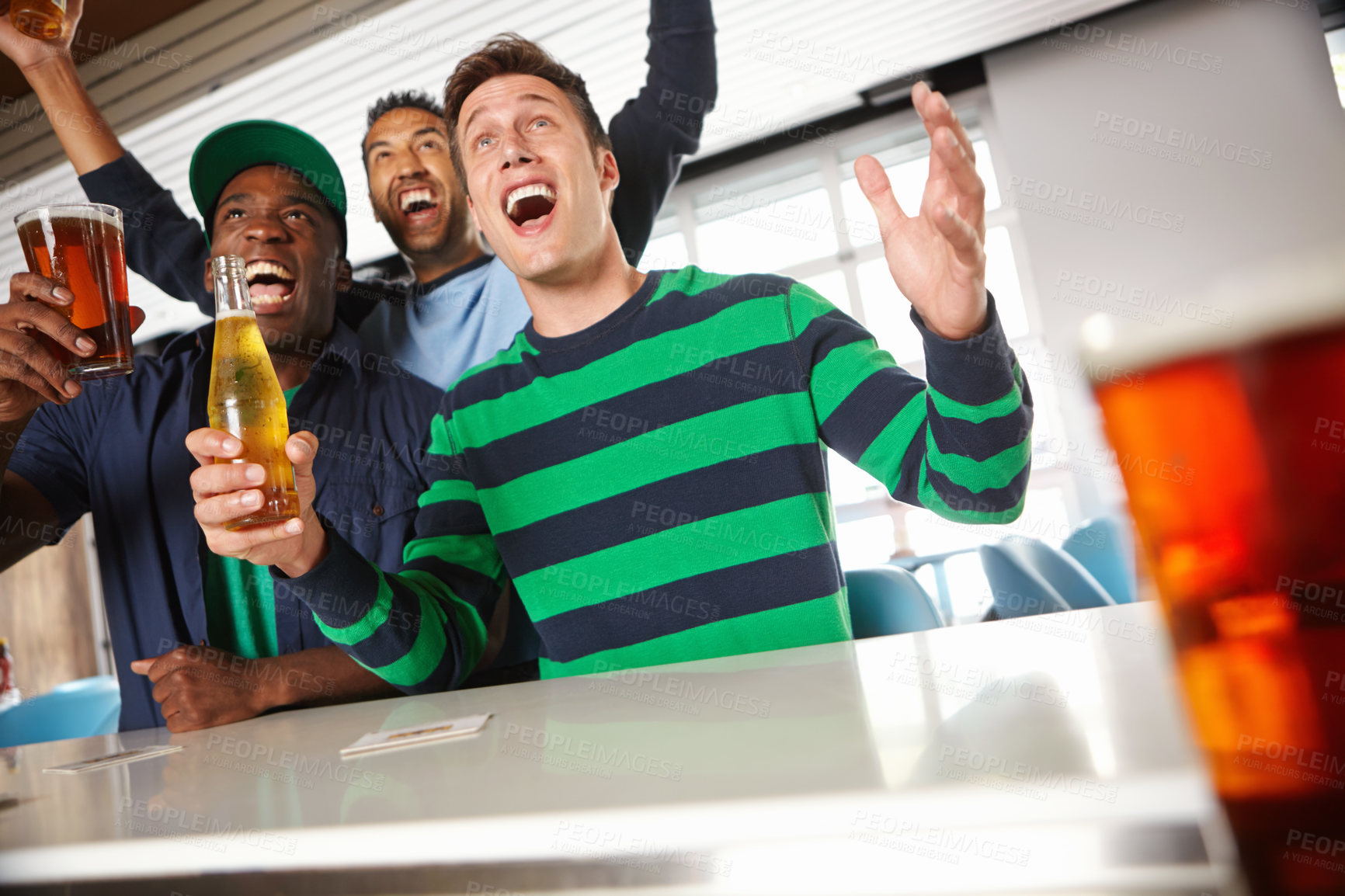 Buy stock photo Low view of a group of friends cheering on their favourite sports team at the bar