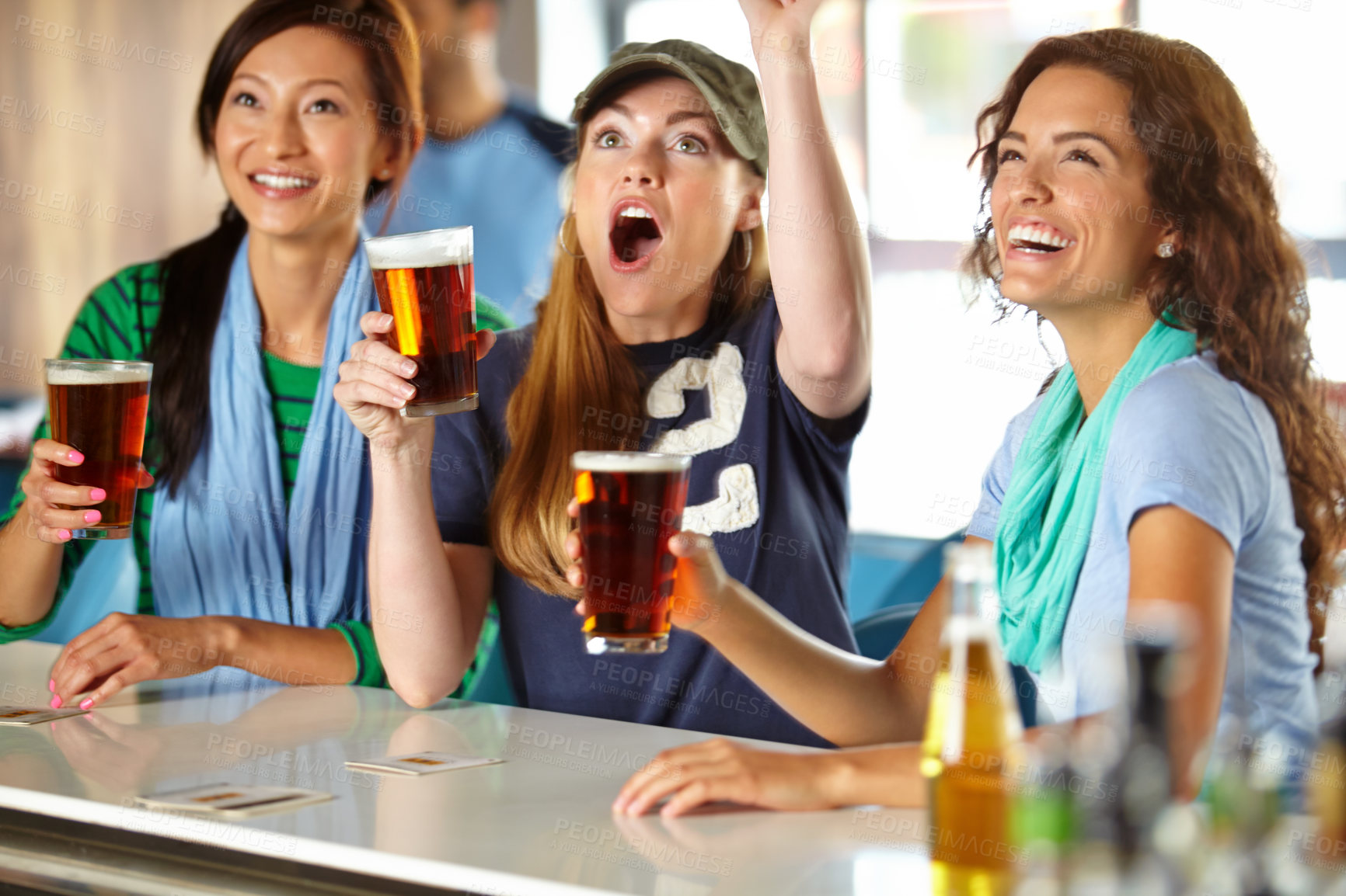 Buy stock photo Three girlfriends kicking back with a few drinks at the bar and watching sport