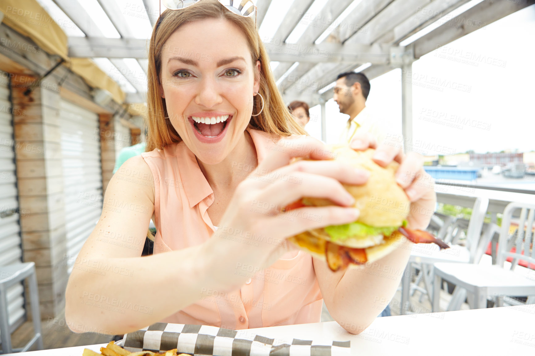 Buy stock photo Portrait of a pretty young woman eating a massive, delicious burger at a restaurant