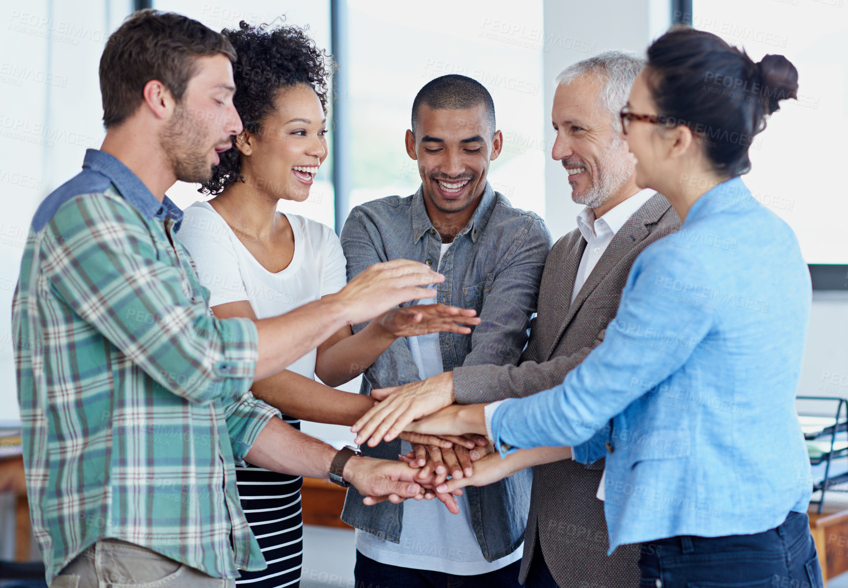 Buy stock photo Shot of a group of happy coworkers standing with their hands together in huddle in an office