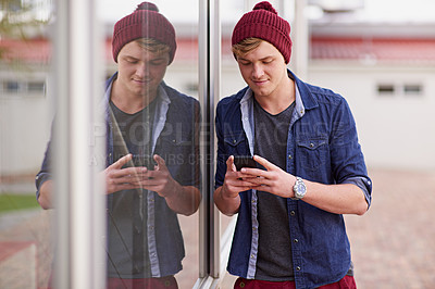 Buy stock photo Cropped shot of a handsome young man using his cellphone on campus