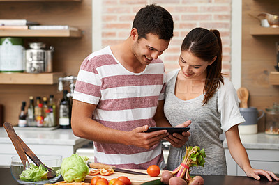 Buy stock photo Shot of a young couple using their tablet in the kitchen