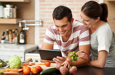 Buy stock photo Shot of an attractive young couple using their tablet in the kitchen
