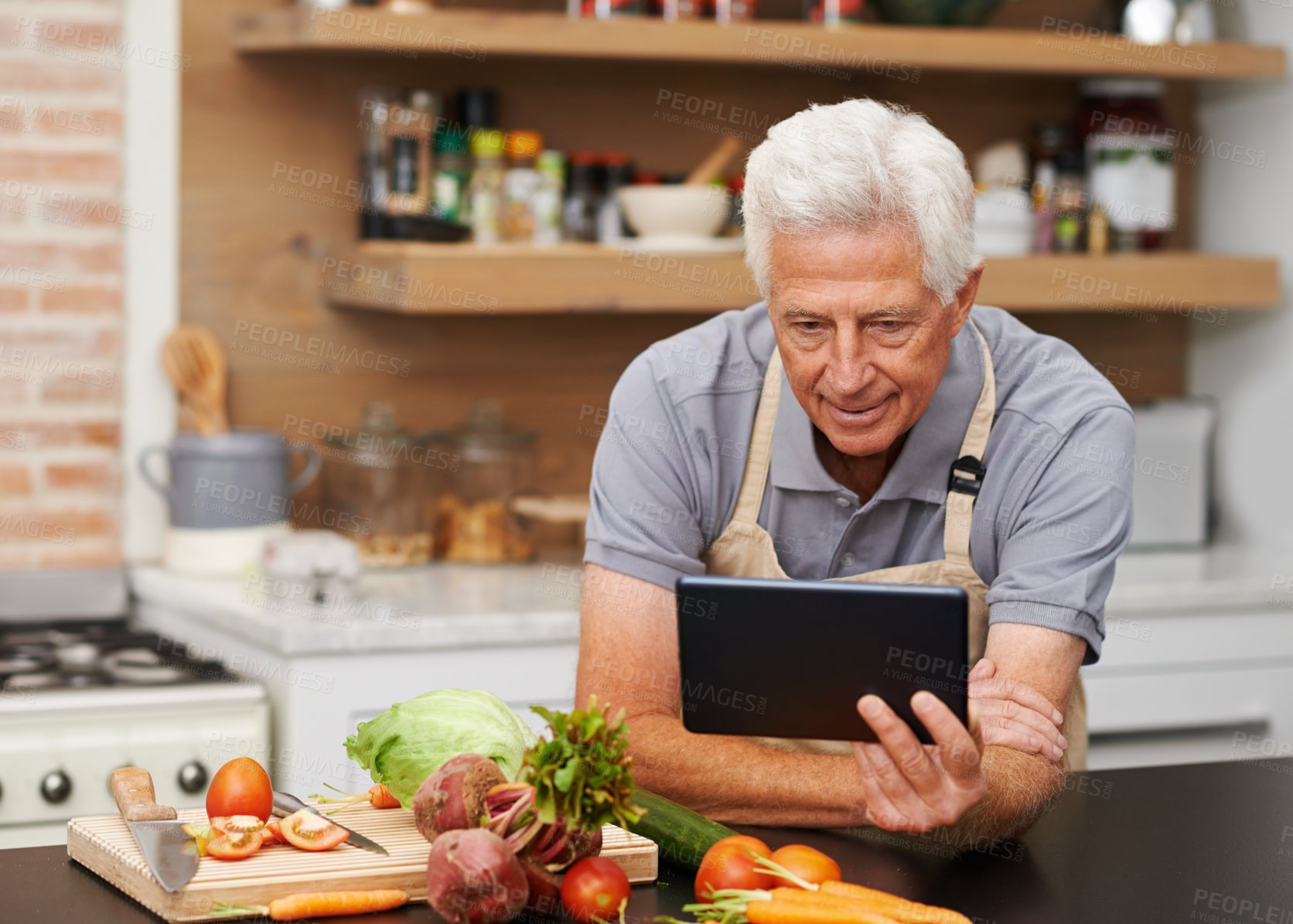 Buy stock photo Shot of a handsome senior man watching a tablet while busy in the kitchen
