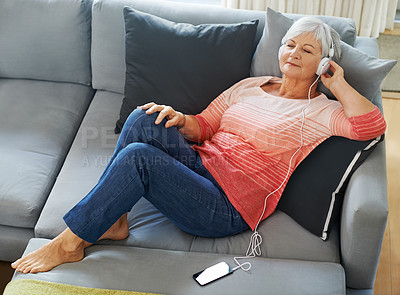 Buy stock photo Senior woman and headphones, music with phone on sofa for relax and rest in living room. Mature, female person and smartphone for listening or streaming podcast on couch for peaceful retirement 