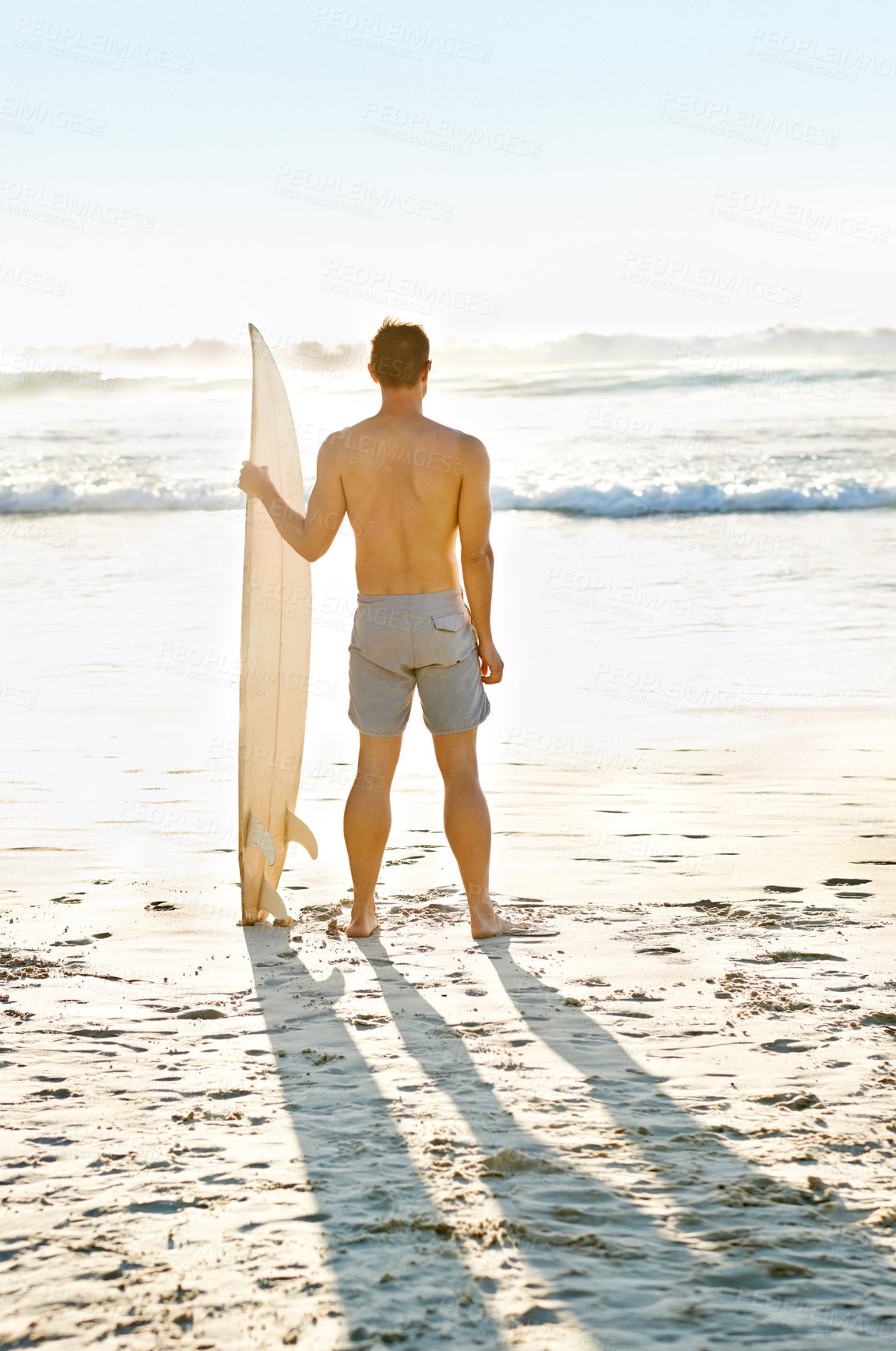 Buy stock photo Rearview shot of a muscular young man holdng his surfboard while on the beach