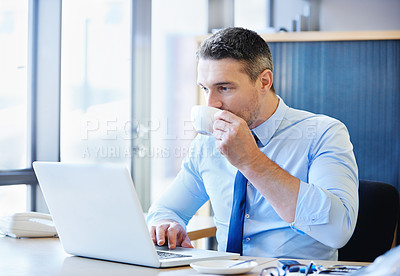 Buy stock photo Shot of a businessman drinking a coffee while working on a laptop in the office