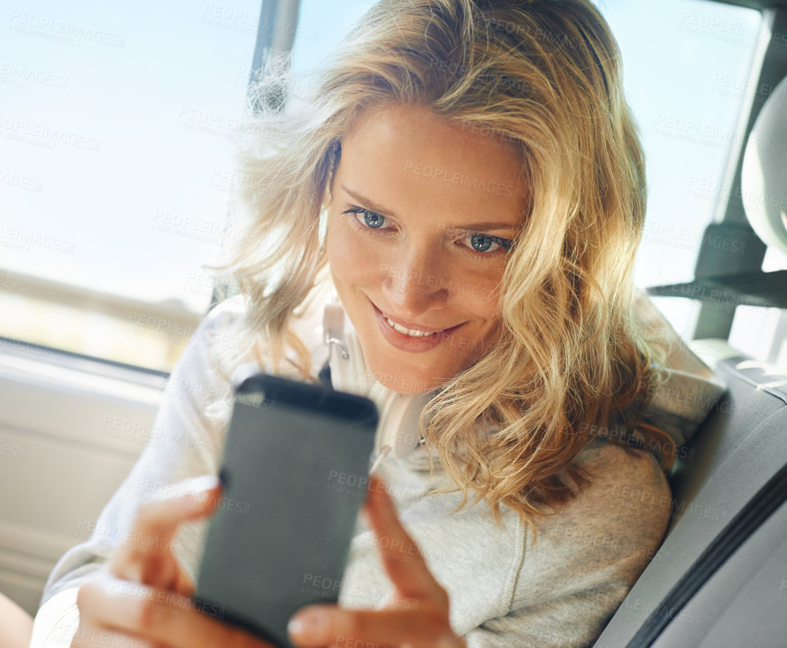 Buy stock photo Shot of a smiling girl taking a self portrait on her phone while she sits in her car