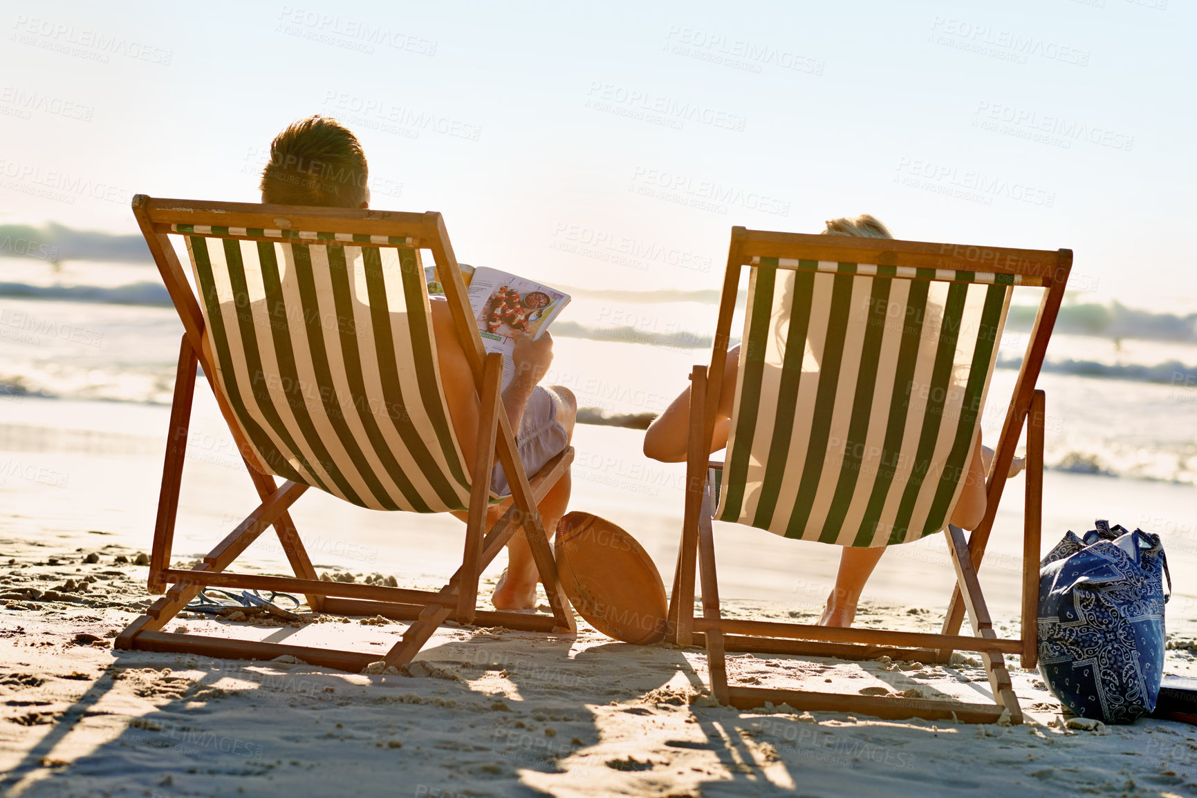 Buy stock photo Back, chair or couple at beach to relax for holiday, vacation or anniversary romance in summer. Travel, magazine or woman on date with man reading newspaper at sea or ocean for wellness in Hawaii