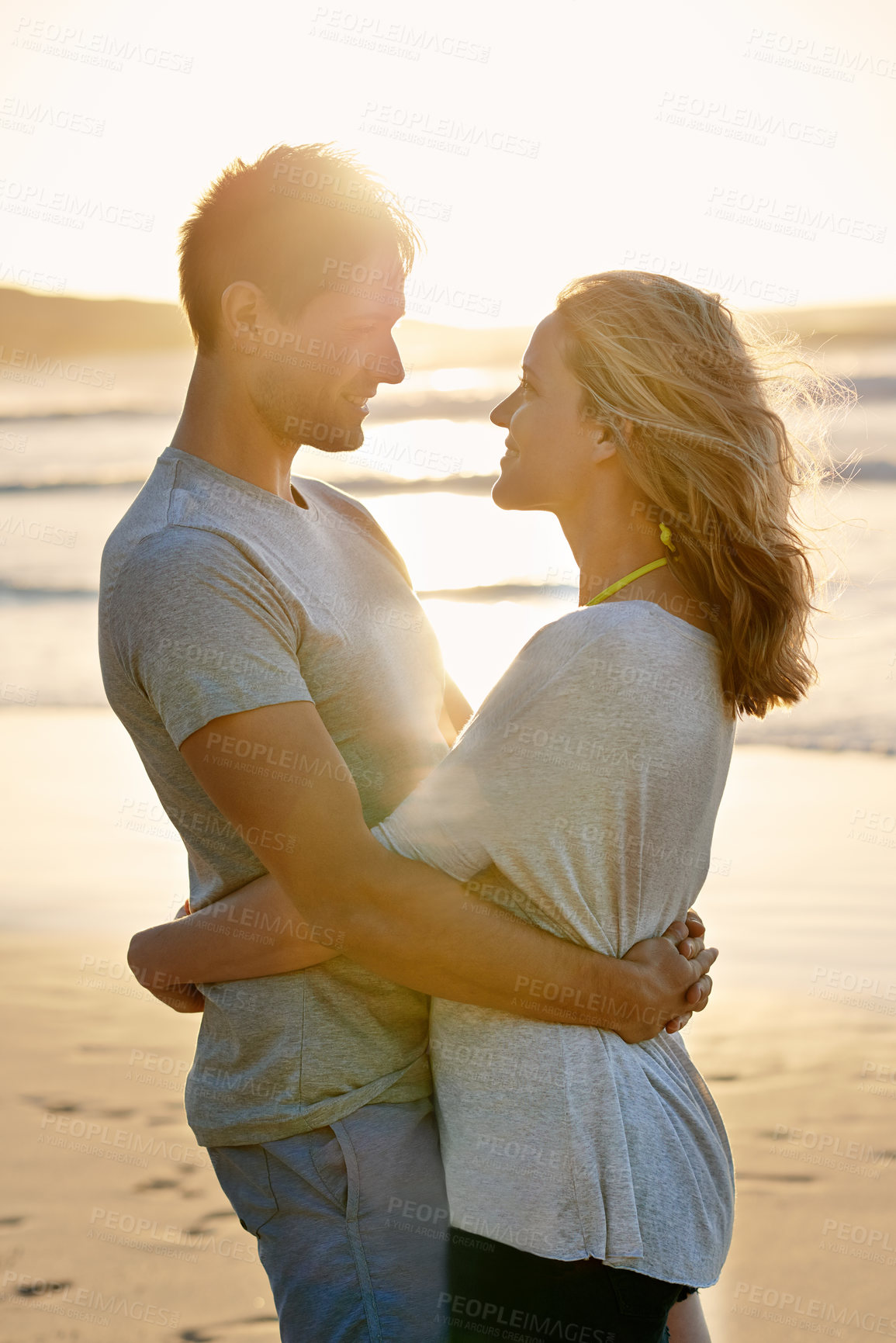 Buy stock photo Lens flare, sunset and hug of couple at beach, ocean and sea with affection, bonding and love in summer. People, partners and romance for care together on vacation, holiday and travel in Australia