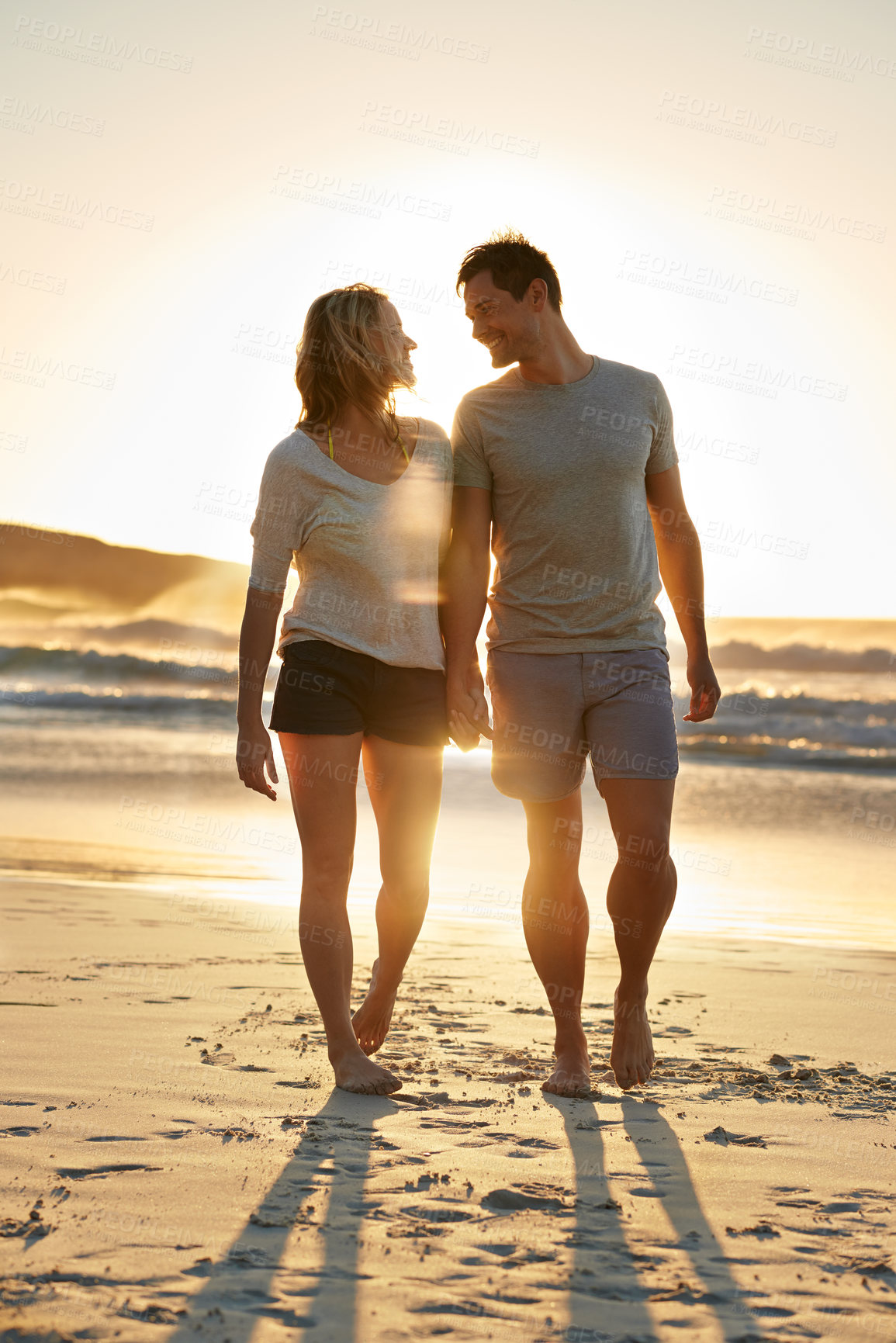 Buy stock photo Shot of a couple walking closely together on the beach at sunset 