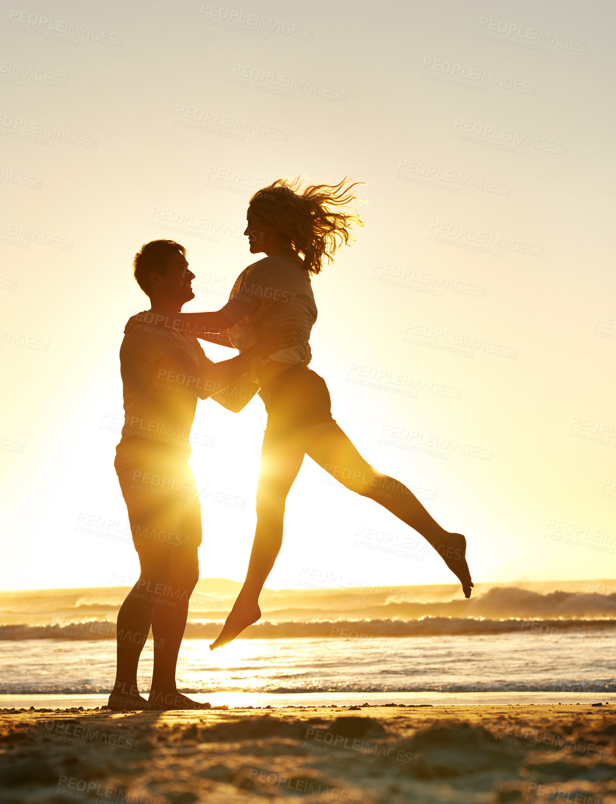 Buy stock photo Lifting, sunset and couple with love at beach, ocean or sea for affection, bonding or for fun with soulmate. People, sunrise and romance for care together on vacation, holiday and travel in Australia