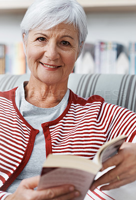 Buy stock photo A senior woman smiling at the camera as she relaxes with a book