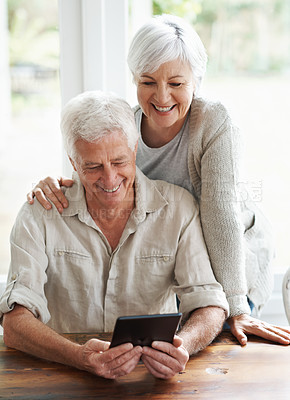 Buy stock photo A senior couple examining a digital tablet as they sit at they dining room table