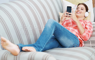 Buy stock photo Happy woman, headphones and streaming with phone in relax on sofa for music, podcast or audio at home. Young female person with smile on mobile smartphone for online entertainment on couch at house