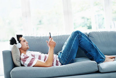 Buy stock photo An attractive man lying on the sofa at home and listening to music 