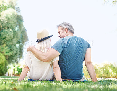 Buy stock photo Rear view of a mature couple embracing one another while sitting on the grass
