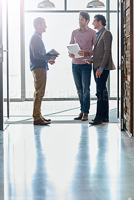 Buy stock photo Shot of male coworkers talking while standing in front of a window in an office