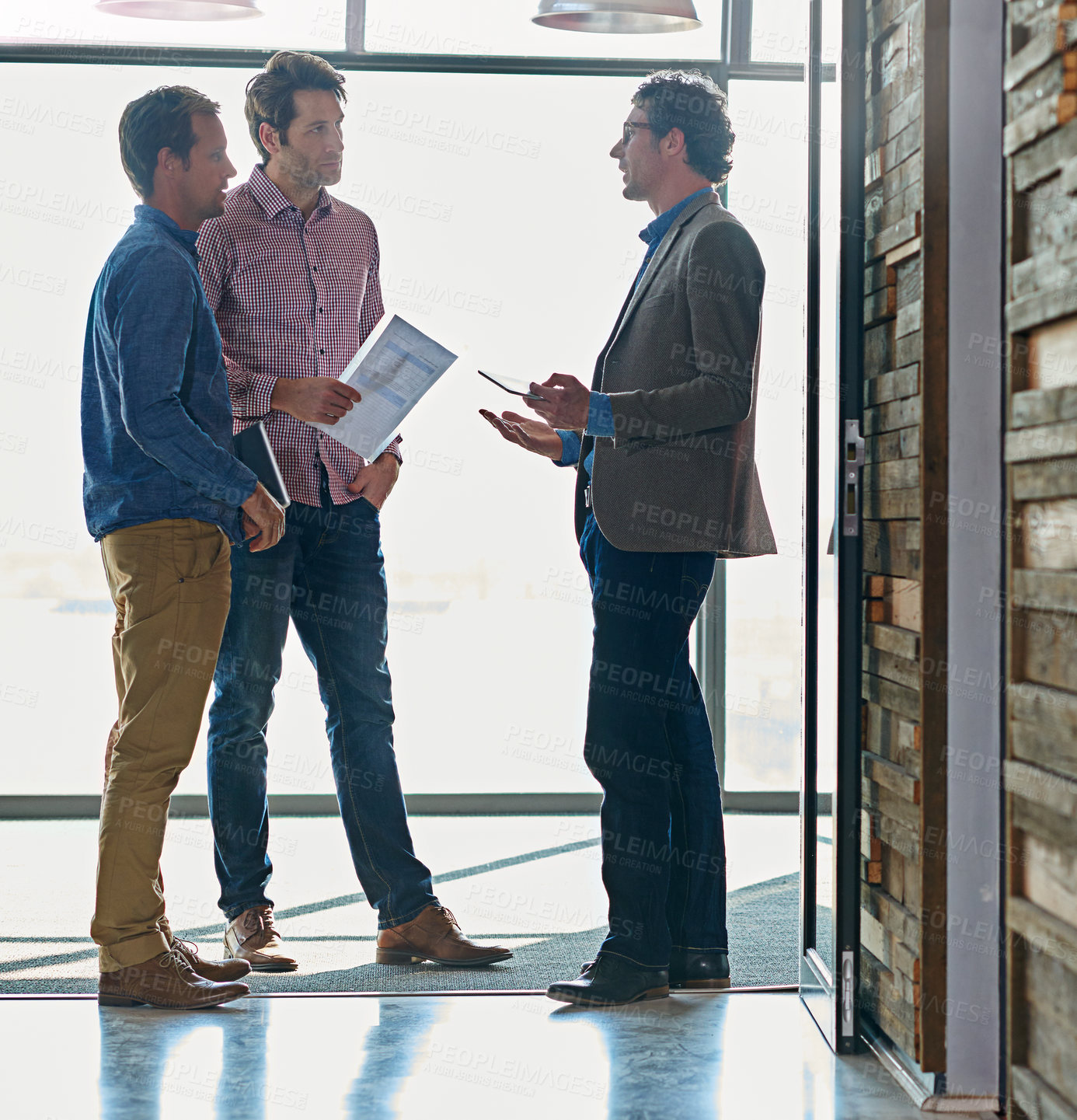 Buy stock photo Shot of male coworkers talking while standing in front of a window in an office