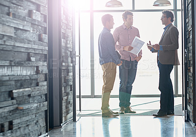 Buy stock photo Shot of male coworkers talking while standing in front of a window in an office