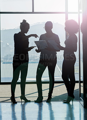 Buy stock photo Silhouette shot of female coworkers talking while standing in front of a window in an office
