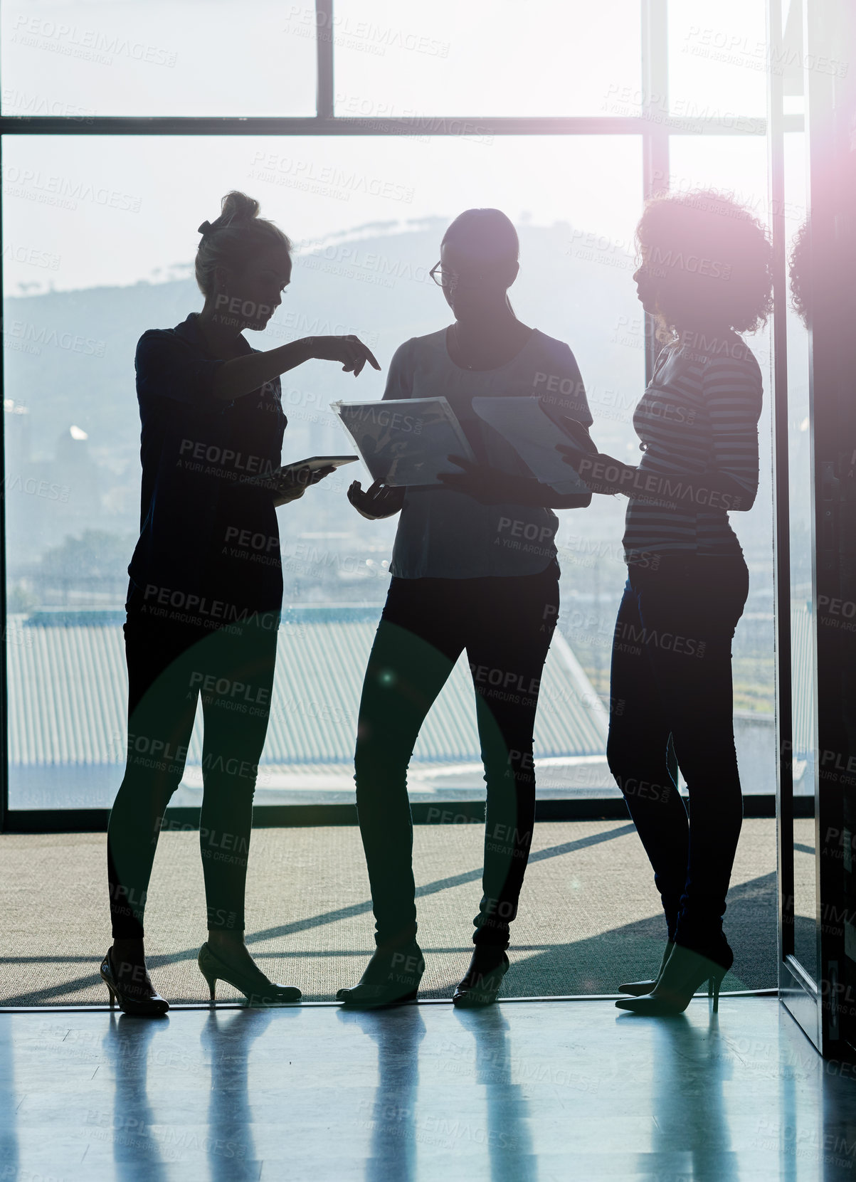Buy stock photo Silhouette shot of female coworkers talking while standing in front of a window in an office