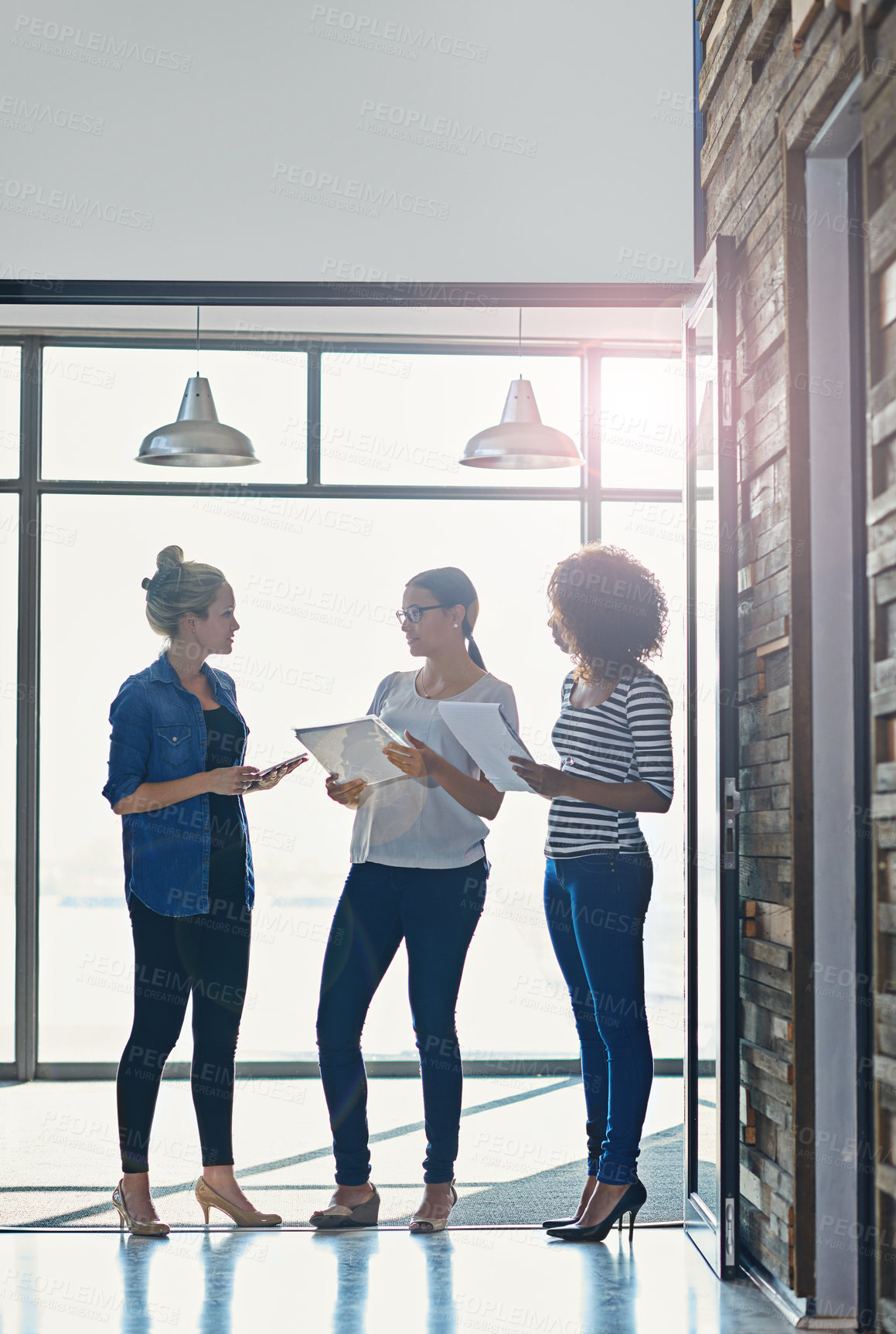 Buy stock photo Shot of female coworkers talking while standing in front of a window in an office