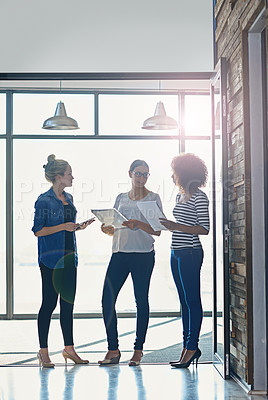 Buy stock photo Shot of female coworkers talking while standing in front of a window in an office