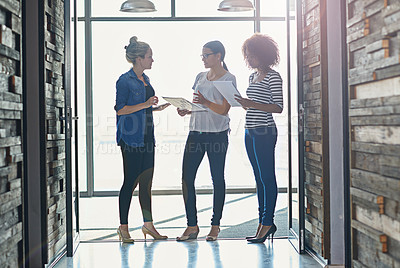 Buy stock photo Shot of female coworkers talking while standing in front of a window in an office