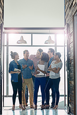 Buy stock photo Shot of a group of laughing coworkers standing in front of a window in an office