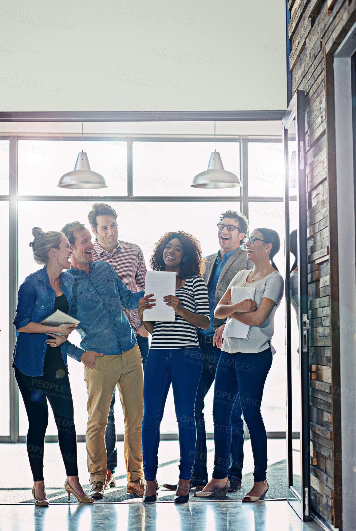 Buy stock photo Shot of a group of laughing coworkers standing in front of a window in an office