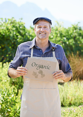 Buy stock photo A mature farmer holding an organic sign while standing outdoors