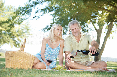 Buy stock photo A happy husband and wife enjoying a glass of wine while having a picnic outside in a park on a summer's day