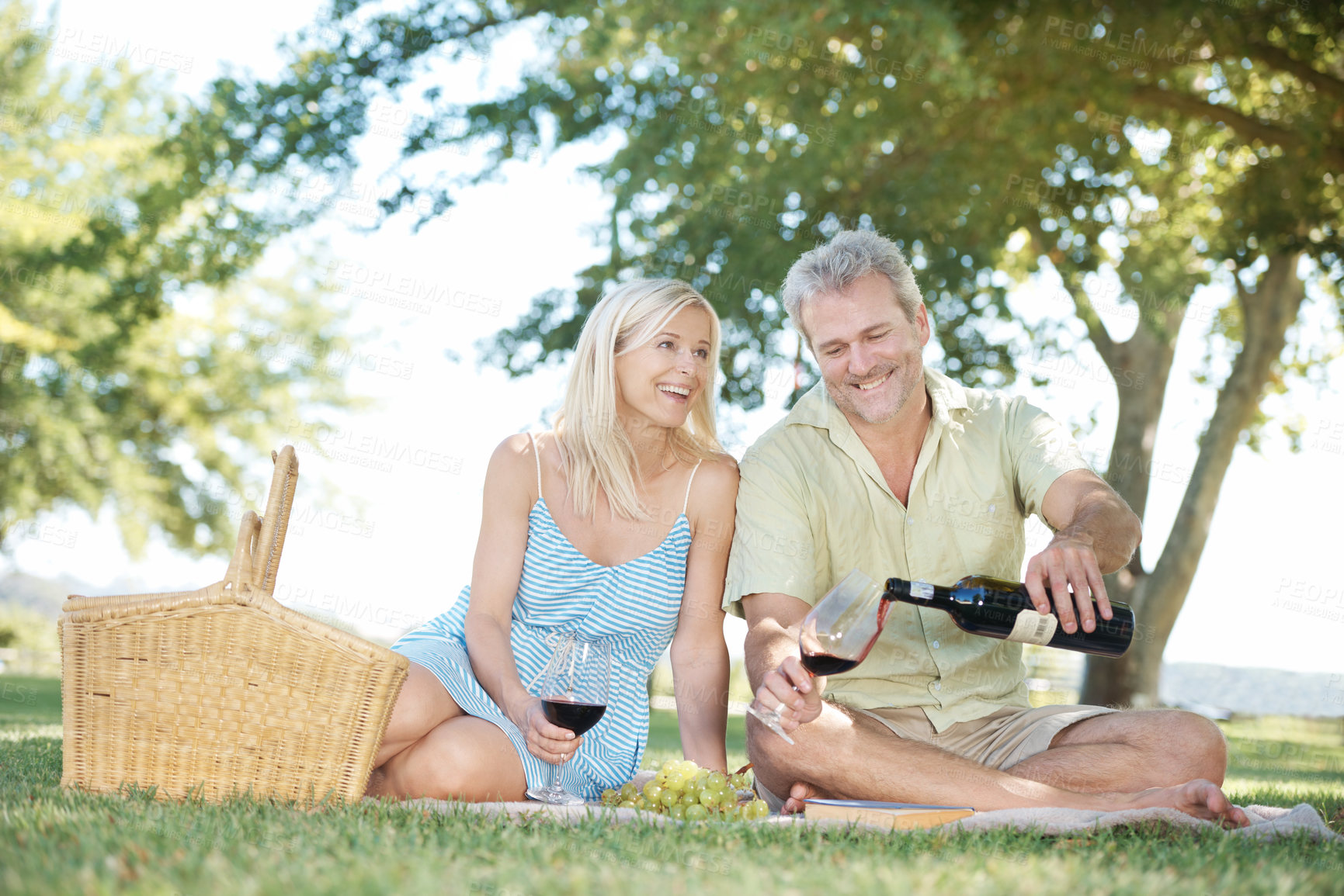 Buy stock photo Happy, couple and red wine with basket on picnic for anniversary, holiday and adventure together. Man, woman and smile with glass at countryside for marriage, love or romantic vacation in New Zealand