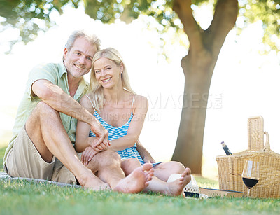 Buy stock photo A happy husband and wife smiling at the camera as they sit in a park having a picnic