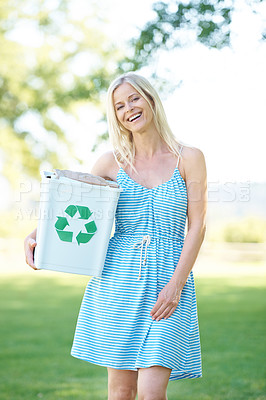 Buy stock photo A beautiful blonde woman standing in a park holding a recycling bin while smiling at the camera