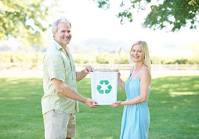 Buy stock photo A happy couple standing in a park holding a recycling bin and smiling at the camera