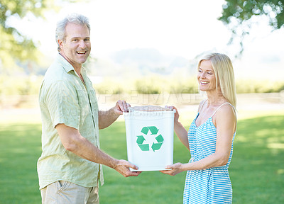 Buy stock photo A happy couple standing in a park holding a recycling bin and smiling at the camera