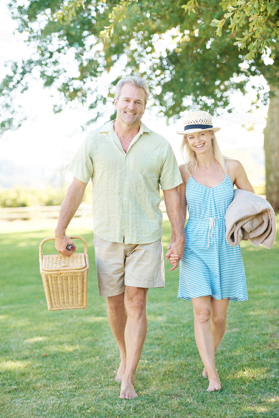 Buy stock photo A happy couple walking in the park looking for a spot to set up their picnic
