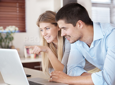Buy stock photo A couple standing in their kitchen looking on a laptop and smiling